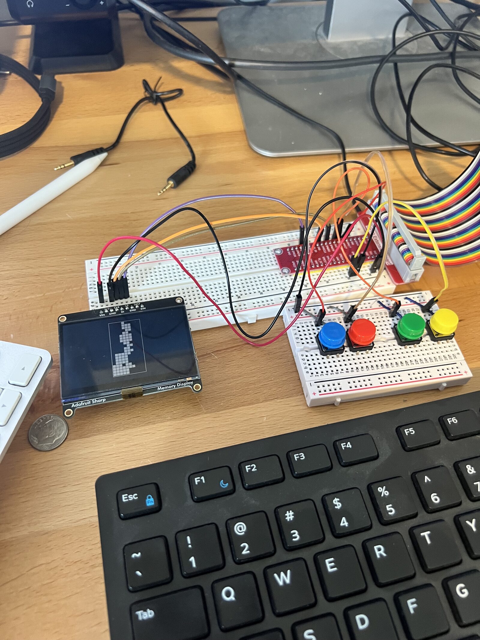 A breadboard with four colored buttons wired to a small display showing a falling-block game