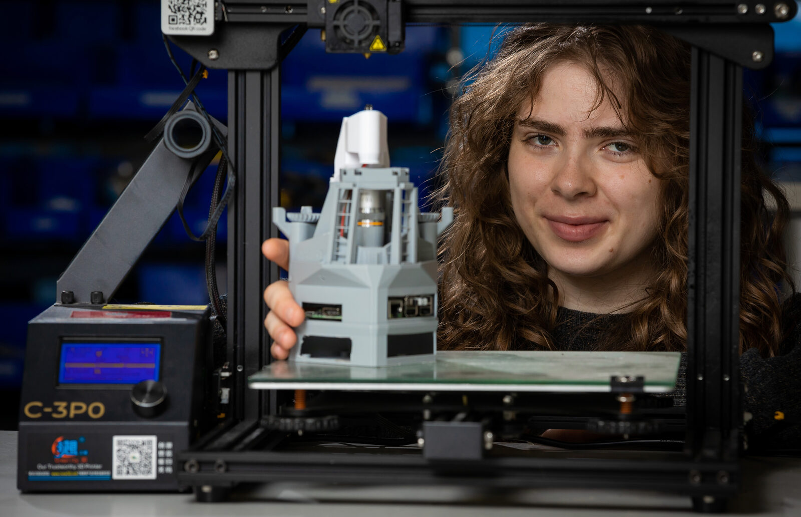 A student holding a freshly printed part at a 3D printer