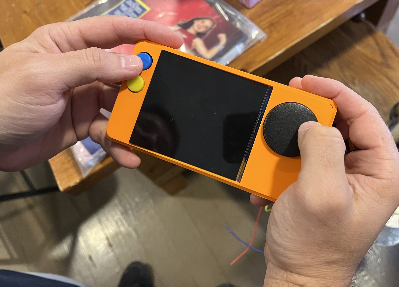 Two hands holding a small orange handheld game console prototype