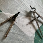Spring dividers and a compass on tracing paper covered in penciled geometric constructions, atop a green cutting mat