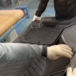 Gloved factory workers pulling freshly molded black rubber car mats off the line, from the car-mat video in this roundup