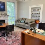 New office in downtown Lexington mid-move-in: couch with a Delve Deeper poster, fireplace, meeting table, and desk